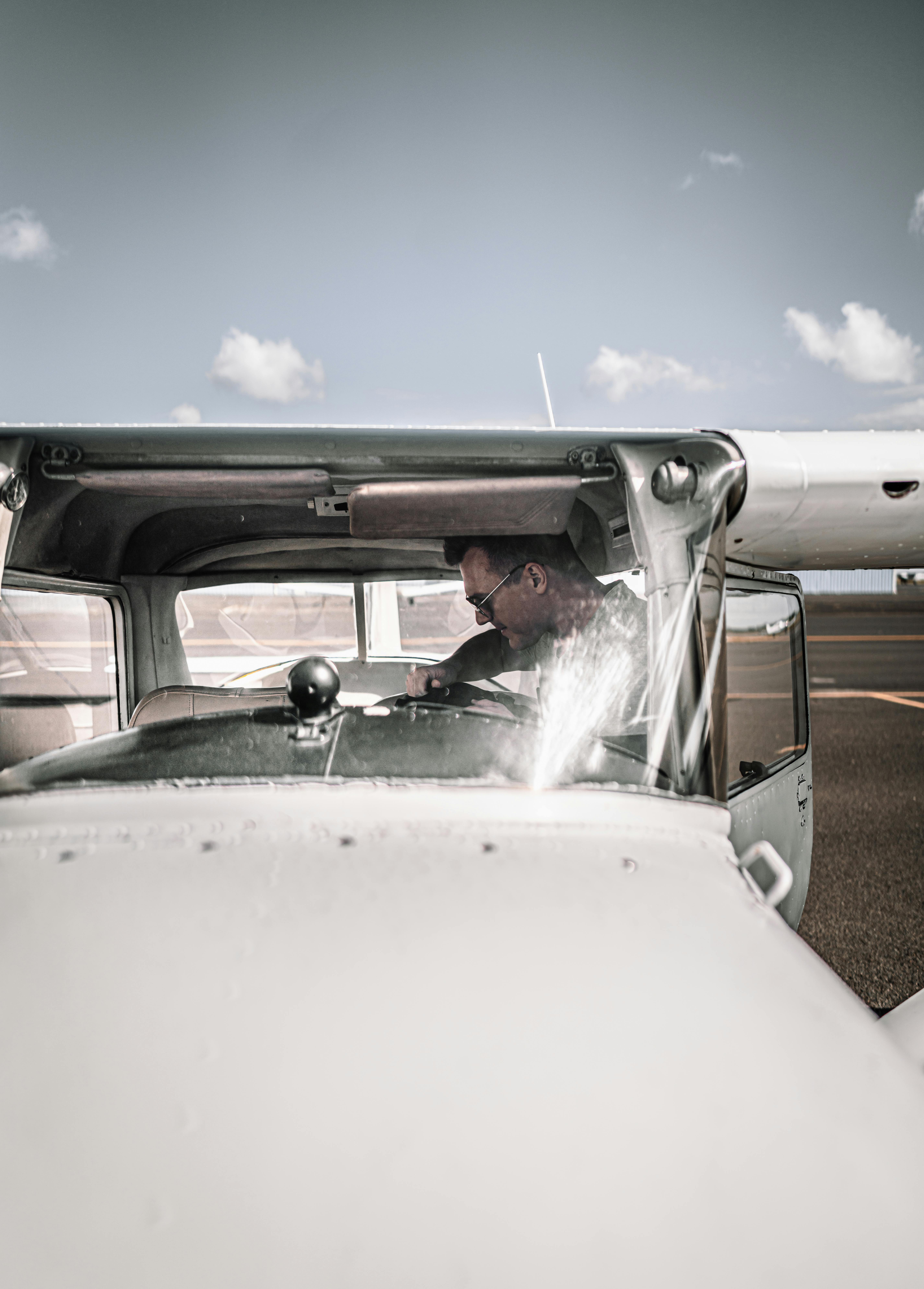 Young male aviator sitting in cockpit of modern light utility aircraft parked on airfield before flight